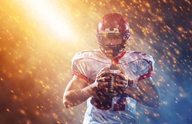 portrait of confident American football player holding ball while standing on the big field with particles effects and lights